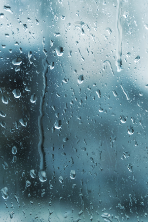 Dirty glass of raindrops on blue background blurredの写真素材