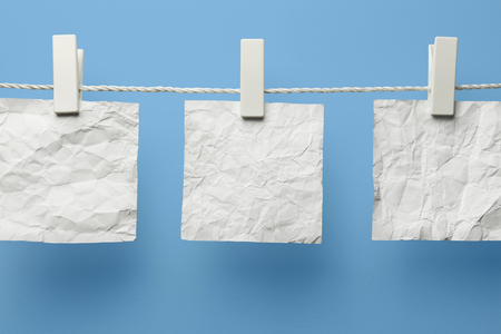 Crumpled paper note hanging with clothespins, light blue wall backgroundの写真素材