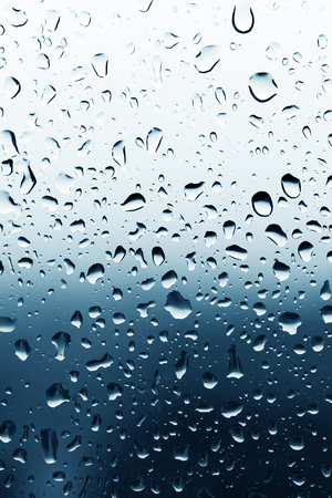 Dirty glass of raindrops on blue backgroundの写真素材