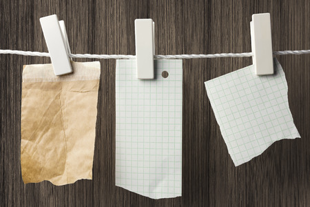 Pieces of note paper hanging with clothespins, wooden board in the backgroundの写真素材
