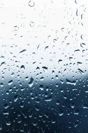 Dirty glass of raindrops on blue backgroundの写真素材