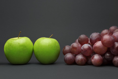 Green apples and bunch of red grapes, isolated on gray