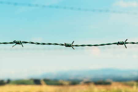 Fence with barbed wire, fields and blue sky on backgroundの写真素材