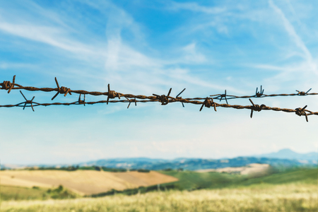 Fence with barbed wire, fields and blue sky on backgroundの写真素材