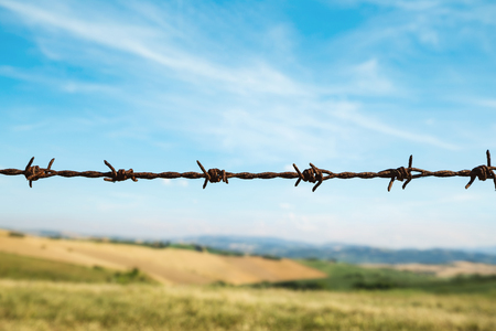 Fence with barbed wire, fields and blue sky on backgroundの写真素材