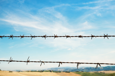 Fence with barbed wire, fields and blue sky on backgroundの写真素材