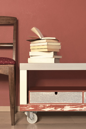 Detail of chair and stack of closed books on the console, red wall backgroundの写真素材