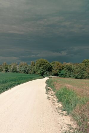 View of rural landscape in spring, white country road and dramatic skyの写真素材