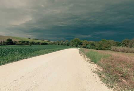 View of rural landscape in spring, white country road and dramatic skyの写真素材