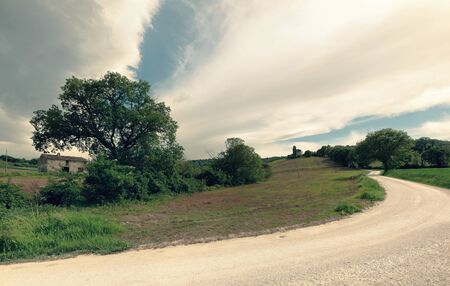 View of rural landscape in spring, white country road and dramatic skyの写真素材