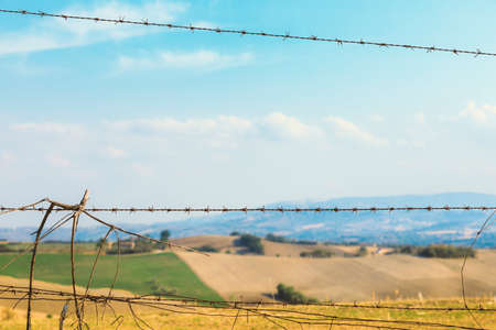 Fence with barbed wire, fields and blue sky