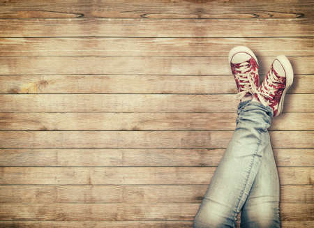 Teenage legs in sport shoes sitting on wooden backgroundの写真素材