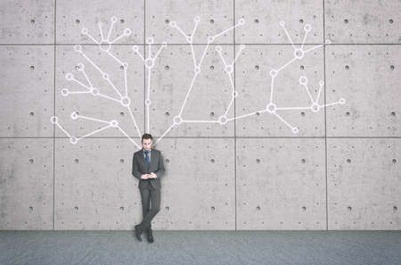 The young businessman with mobile phone next to a wall with a network system behind him.