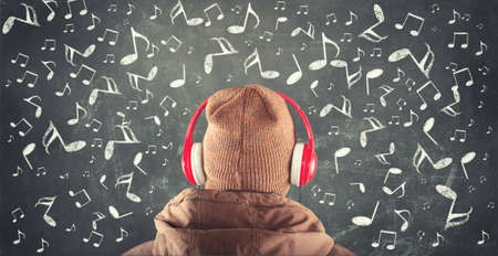 Teenager standing in front of a blackboard with musical notes drawn around and listening to music on headphonesの写真素材