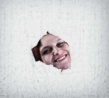 Happy girl smiling through a broken wall, close upの写真素材
