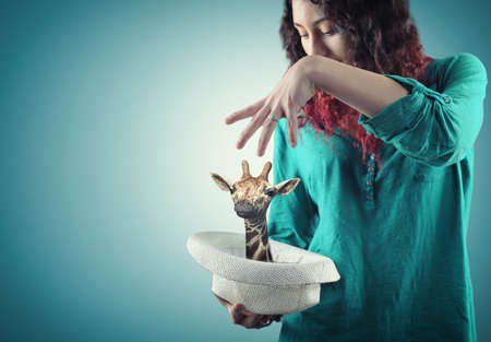 Young girl making a magic trick, giraffe show up in hatの写真素材