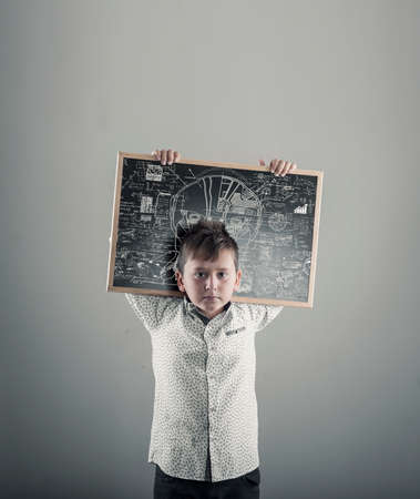 Kid holding a sketch of a robot and physics formulas on blackboardの写真素材