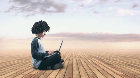 Teenager man sitting on a wooden floor and using a laptopの写真素材