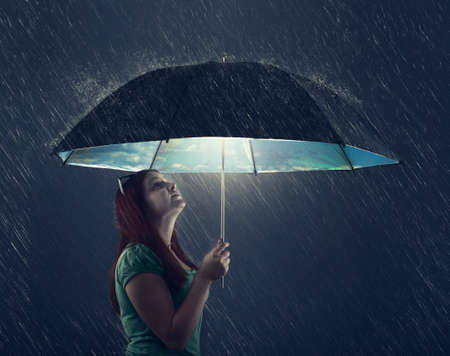 Young woman under an umbrella, protected from rain on black backgroundの写真素材