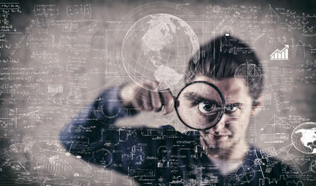 Man looking through magnifying glasses to mathematical formulas and problems.の写真素材