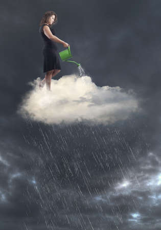 Woman in black dress standing over a cloud creating rain with watering canの写真素材