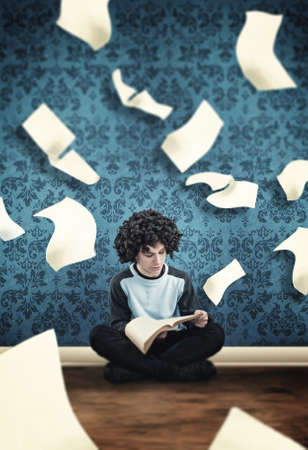 Young guy reading a book with flying sheets coming out of the book in a room.の写真素材