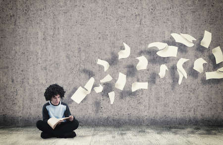 Young guy reading a book with flying sheets coming out of the book