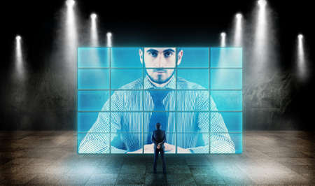Young businessman looking at a big screen and talking to hologram.の写真素材