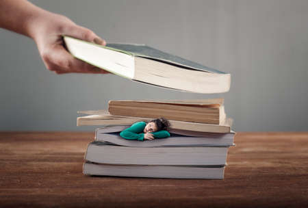 Scared woman in the middle of books is crushed by another one.の写真素材
