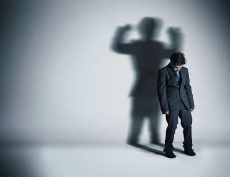 Image of a weak businessman standing depressed in front of a wall and his shadow shows streght.の写真素材