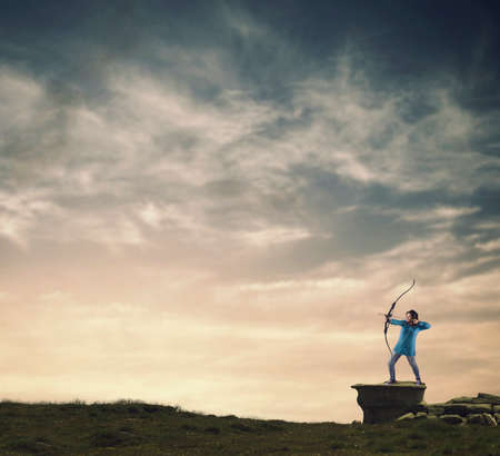 Woman shooting with a bow on a rock at sunset.
の写真素材