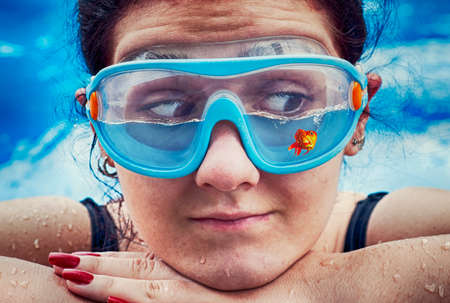 Young woman wearing swimming glasses half filled with water and a fish .の写真素材