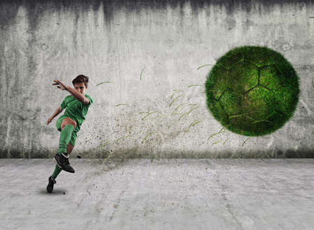 Soccer pckgrlayer shooting a ball of grass, in a urban background.の写真素材