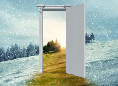 Opened door on a field during winter which leads to a warmer season. Changing season through the door concept.の写真素材