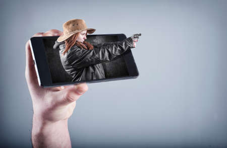 Hand holding a smartphone which displays a movie on touch screen.Cowboy girl gun shoot and get out of the screen.の写真素材