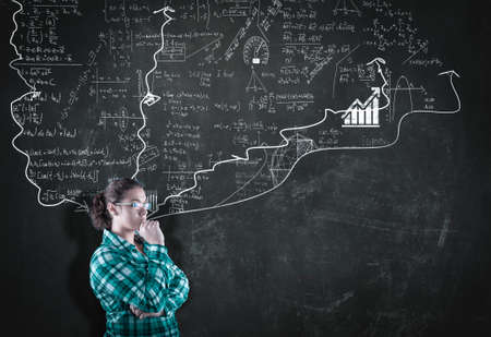 Thoughtful woman next to a chalkboard drawn with math formulas. The concept of making a plan.の写真素材