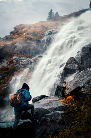 Traveler with a backpack climbing on a mountain near a waterfall.の写真素材