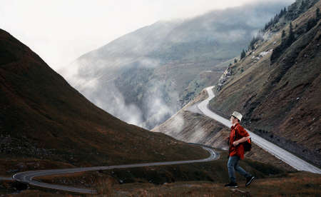 Young traveler walking on a hilld with mountains crossed by roads in the background.