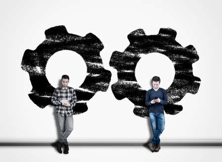 Two man using phone against a white wall painted with engine gear mechanism. The concept of working...