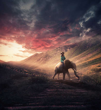 Woman rides an elephant on the mountains at sunset.の写真素材