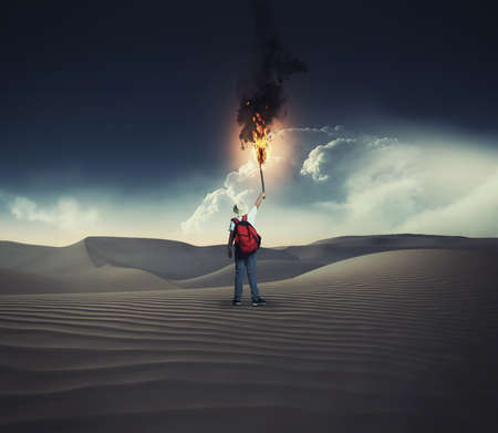 Young traveler holding a torch with fire in the desert.