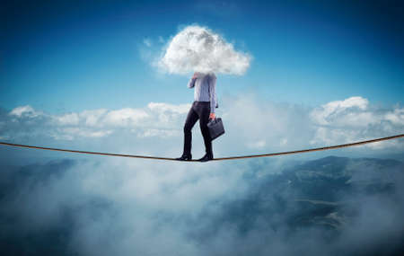 Businessman walks on a rope at high altitude above mountains and clouds . Head covered by a cloud.の写真素材