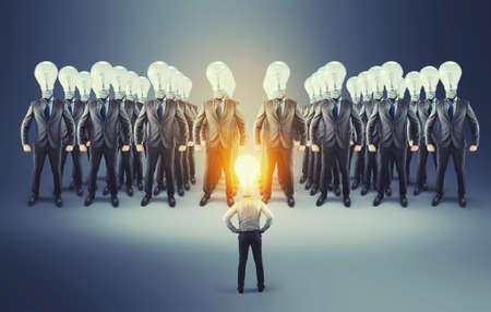 Businessman with lit lightbulb instead of a head standing in front of business team. Lower employee business meeting.の写真素材
