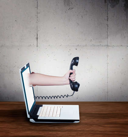 Hand holds an old telephone receiver and reaches out of the laptop screen. Online call .