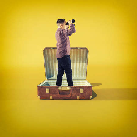 Men looks through binoculars standing in a opened luggage