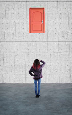 Confused woman looks up to a closed door in the wall.の写真素材