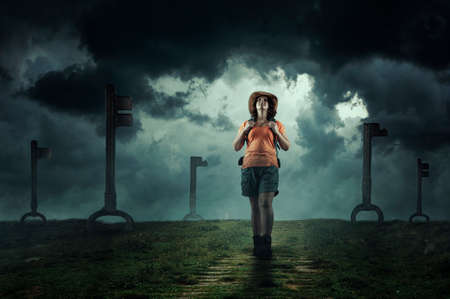 Woman with a backpack walking on a dark and moody field . Old keys standing in the ground . Key to success and journey of life. Many opportunities .の写真素材