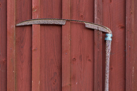 An old frayed scythe hanging on a red painted barn wallの写真素材