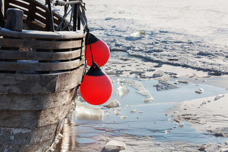 Old wooden boat with red fenders surrounded by iceの写真素材
