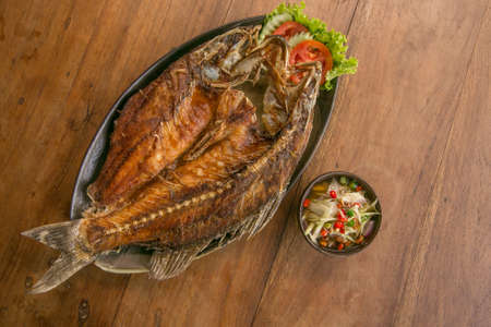 Deep fried whole fish crispy and delicious spicy sauce on a wood table - asian cuisineの写真素材